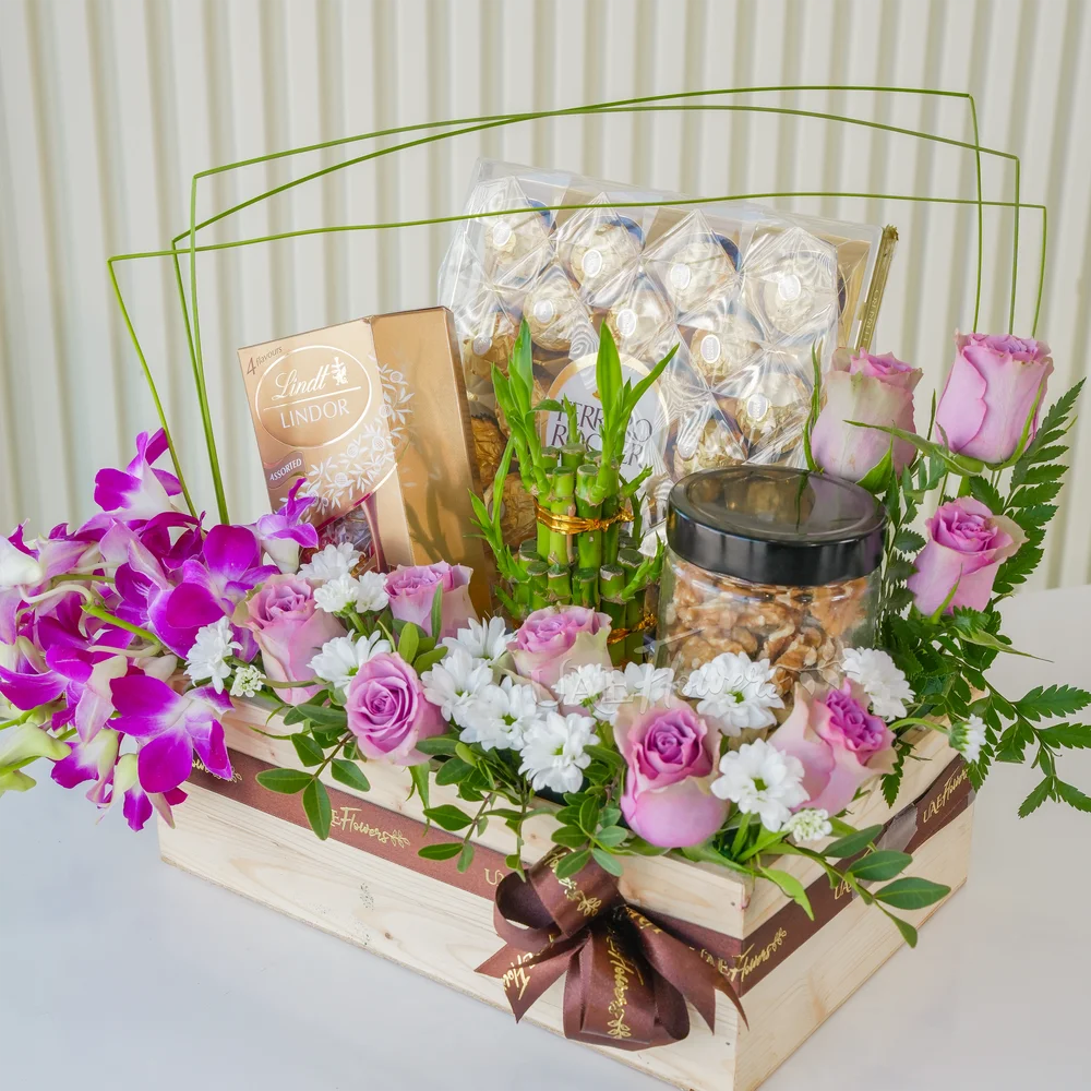 A wooden box arrangement of 10 pink roses, 5 purple orchids, white chrysanthemums, 250Gms of walnut in jar, 2 layer lucky bamboo, 24pcs of ferrero rocher chocolate and lindt lindor assorted chocolate box 200gms with green fillers.