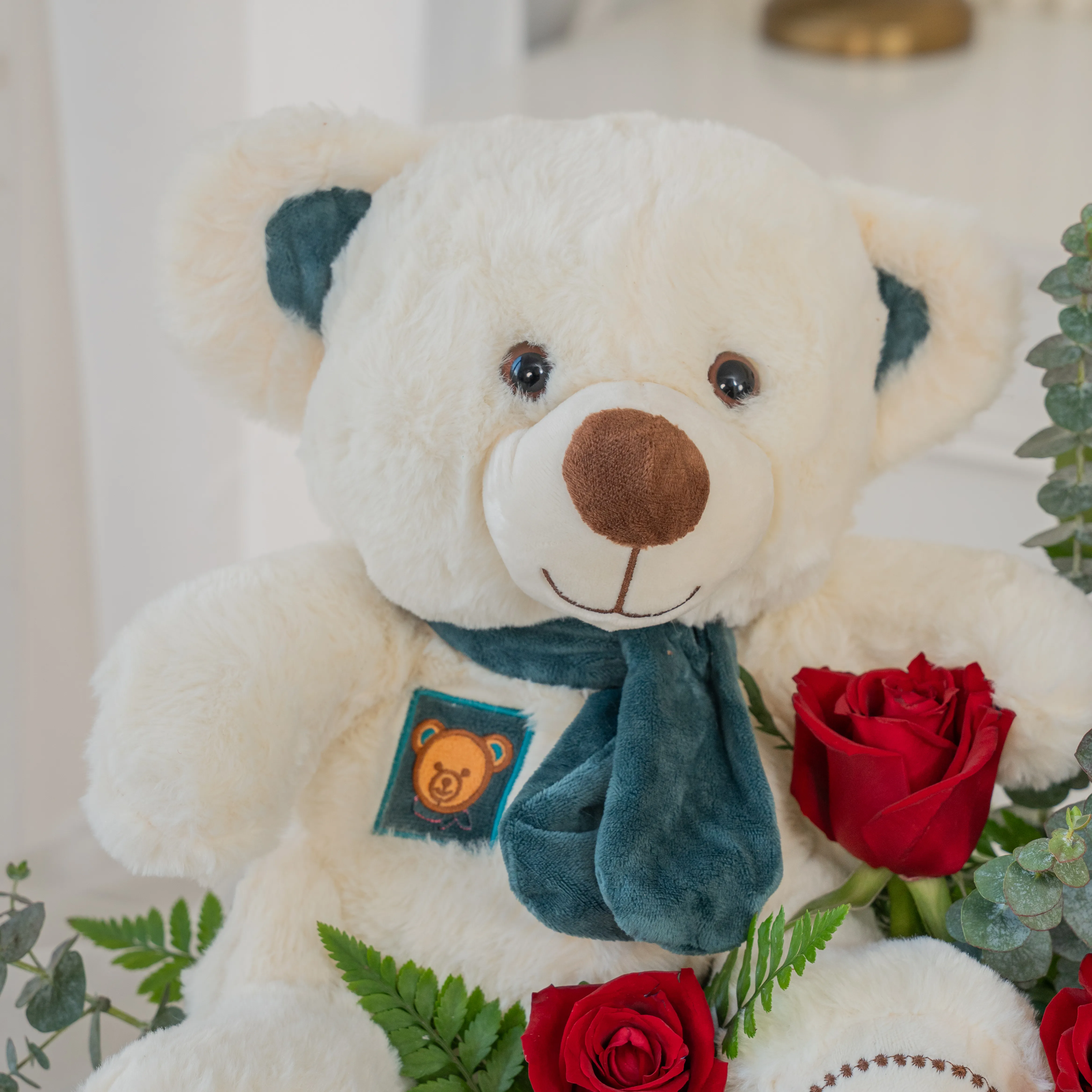 Basket arrangement of 20 red roses and small white teddy bear with eucalyptus leaf and green fillers.