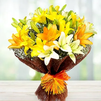 A bouquet of 3 white lilies, 3 orange lilies and 3 yellow lilies in brown wrapping paper tied with a orange ribbon