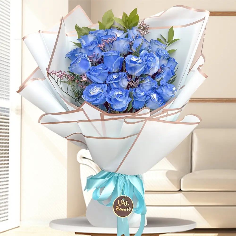 A bouquet of 24 blue roses with fillers in white wrapping paper tied with a blue ribbon