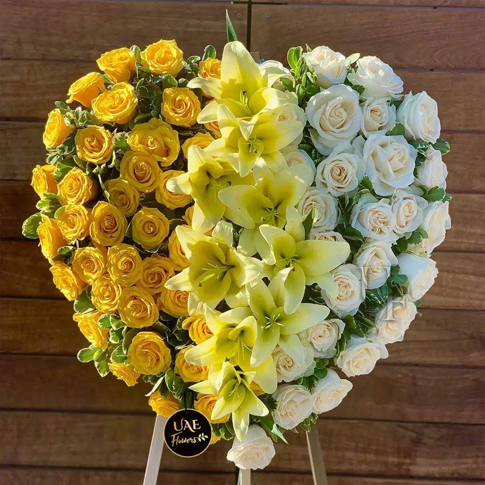 A heart shaped floral arrangement of yellow roses and lilies with white roses on a stand, best for events.