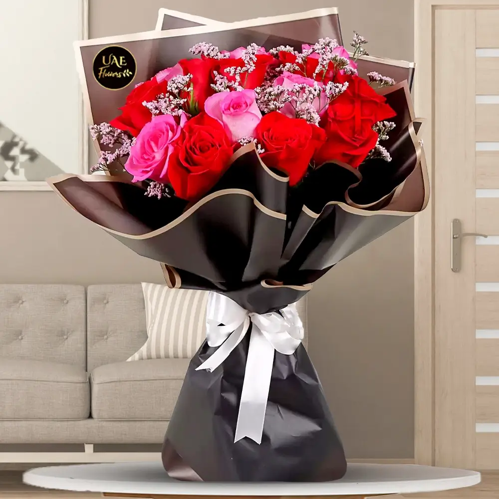 A bouquet of 15 red and pink roses with limonium fillers, in black wrapping paper tied with white ribbon