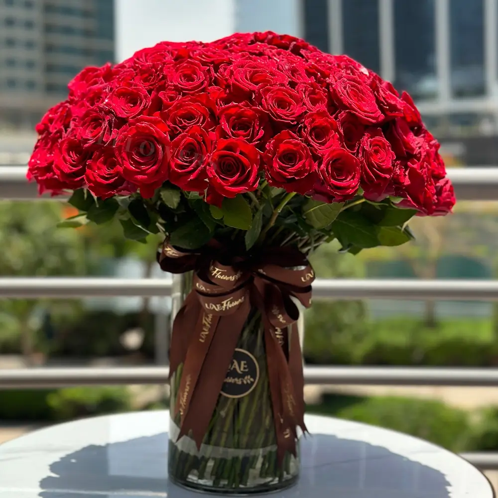 100 red roses and green fillers in a glass vase, beautifully tied with ribbons