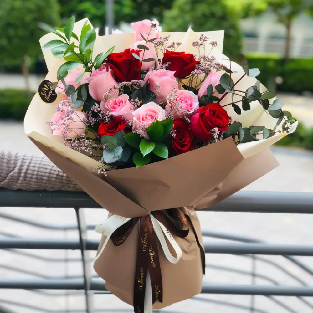 A bouquet of 6 pink roses and 6 red roses with eucalyptus leaf and green fillers in brown and white wrapping paper tied with brown ribbon
