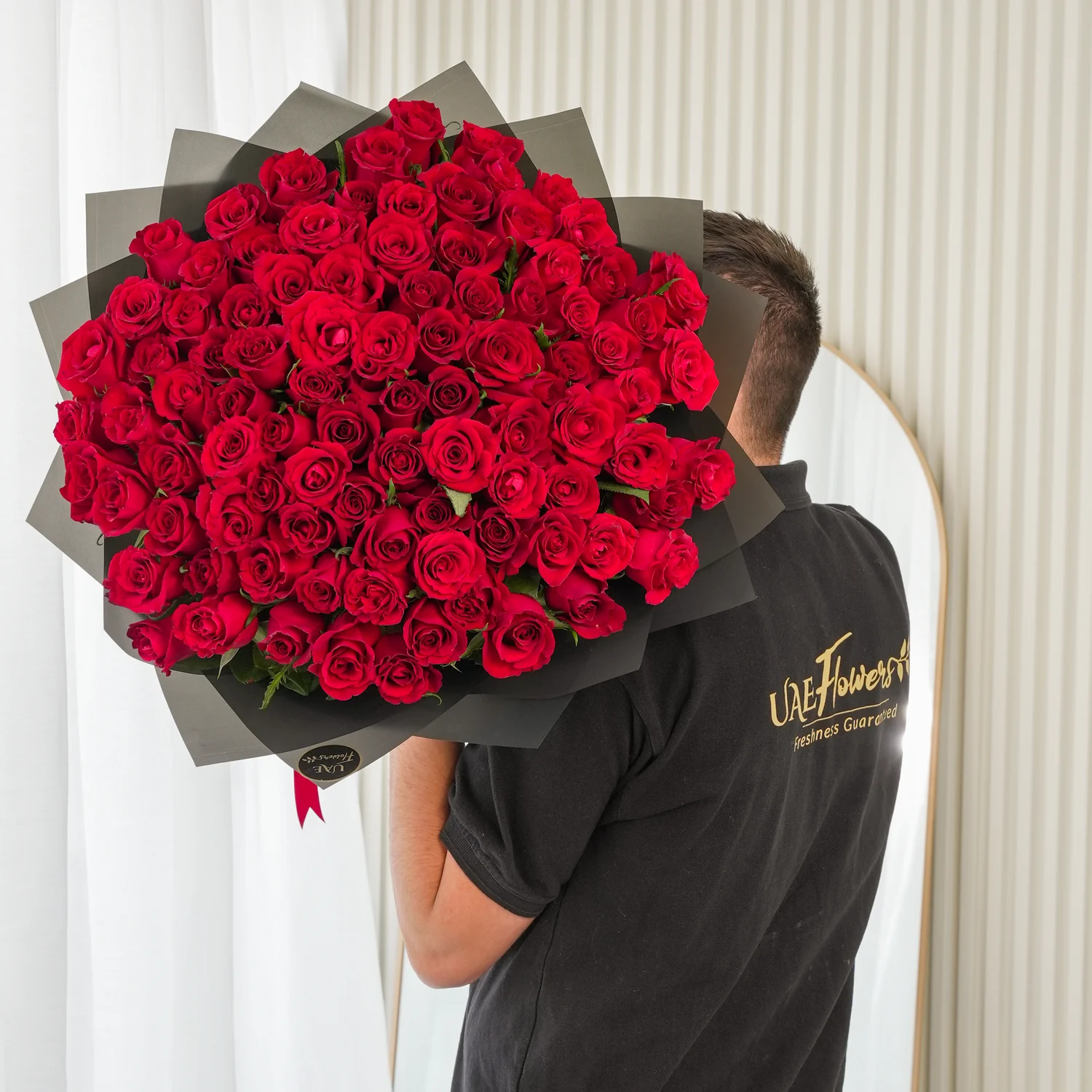 100 premium red roses hand-tied with green fillers and wrapped in black paper with satin ribbon