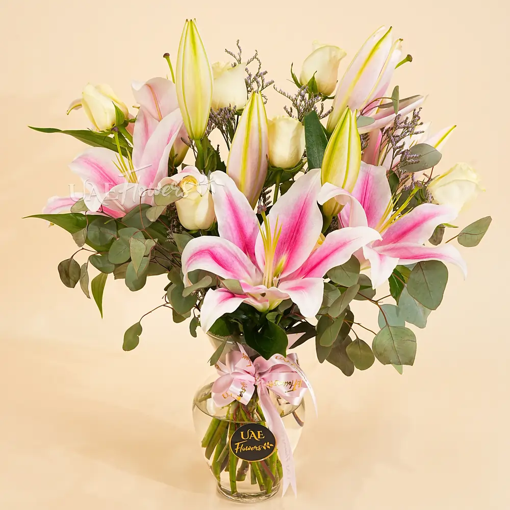 4 Pink lilies & 10 white roses in a cylindrical glass vase with eucalyptus leaves as fillers