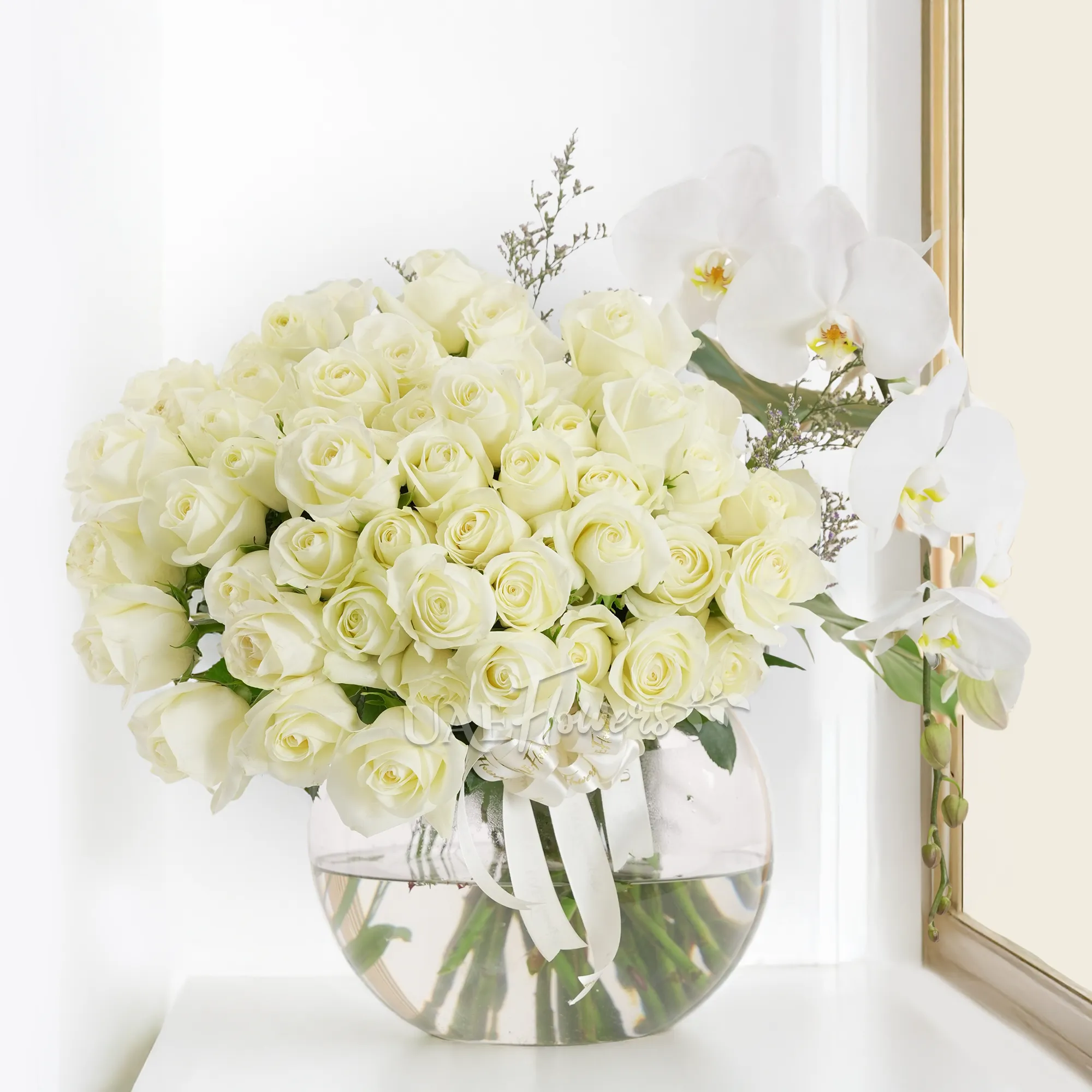 Glass vase of 50 white roses with white orchid and limonium fillers tied with satin ribbon