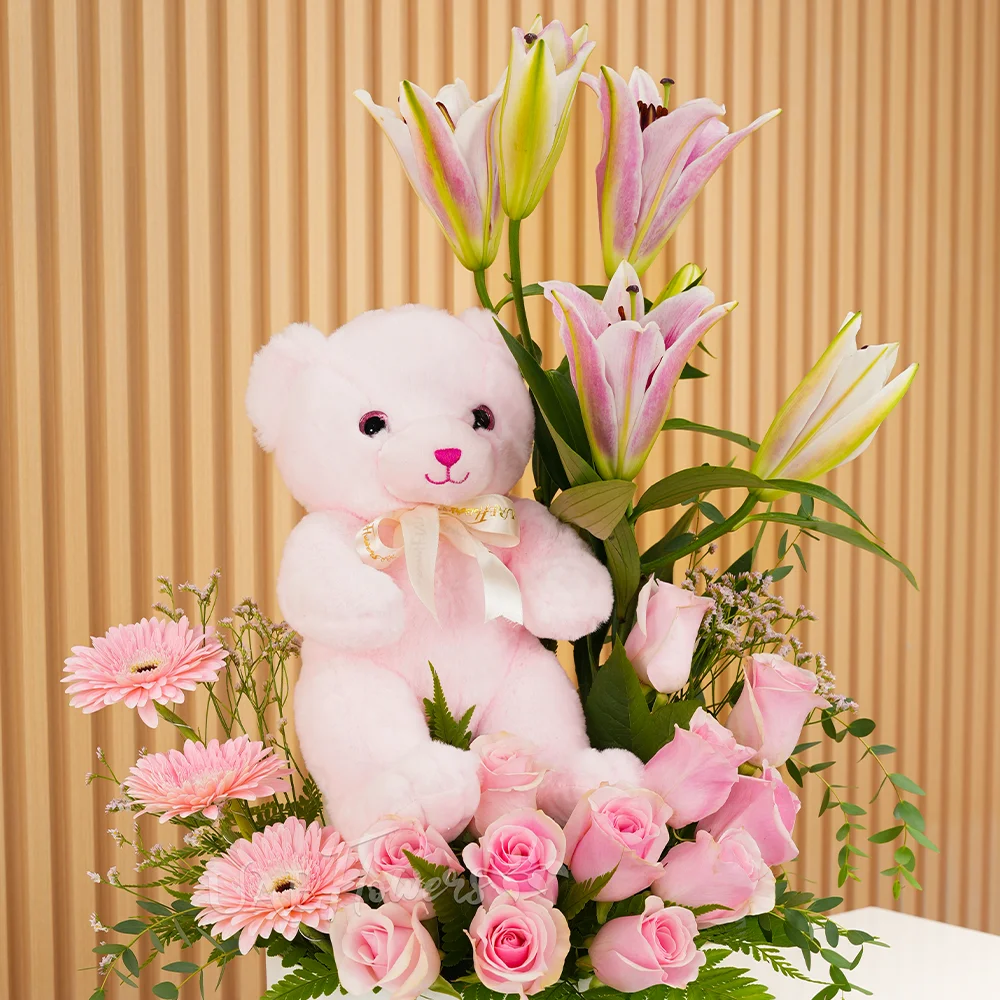 pink lily, pink gerberas, and pink roses in a round white box with a small pink teddy bear