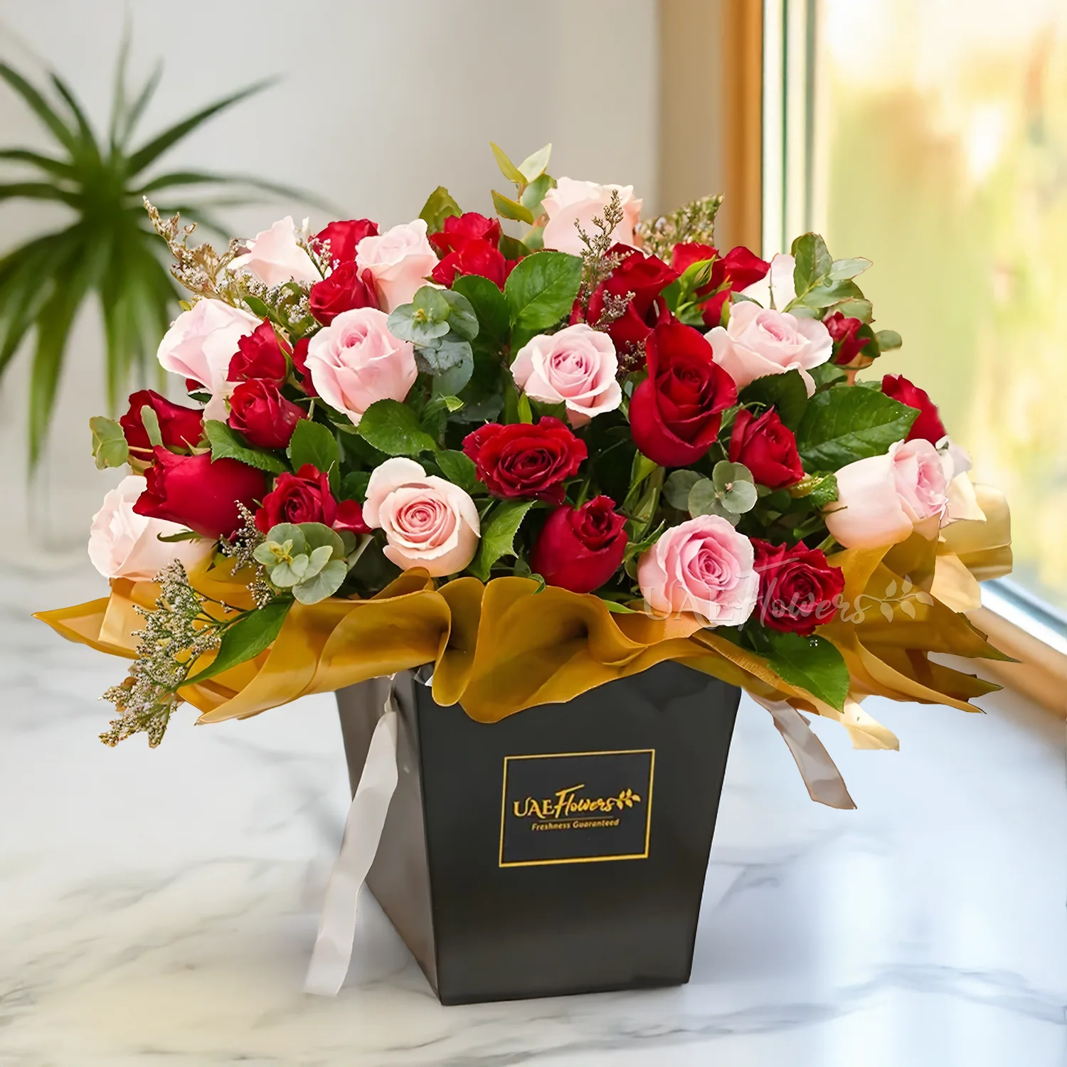 An arrangement of 30 red roses and pink roses with green fillers, eucalyptus leaf, and limonium fillers in a black box